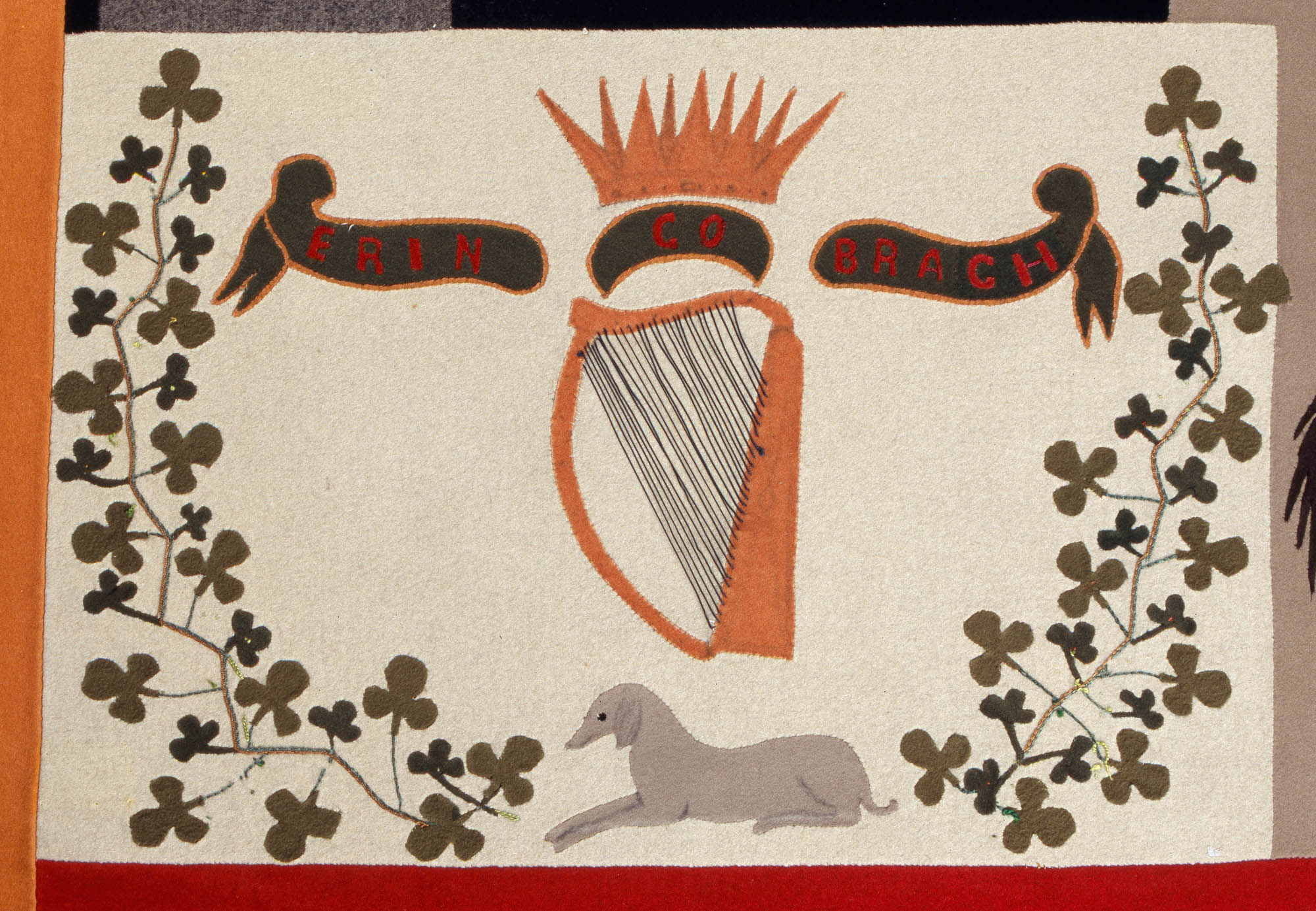 20060619_NMIDT-1960-42_Stokes_detail_18_cr1_2000px-(5).jpg Close-up of a panel on the Stokes Tapestry depicting a harp and crown in the middle with springs of shamrocks on either side. There is a banner that reads "Erin Go Bragh" in the middle and a wolfhound lying down on the bottom.